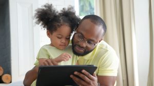 Father and child cuddle together looking at a tablet