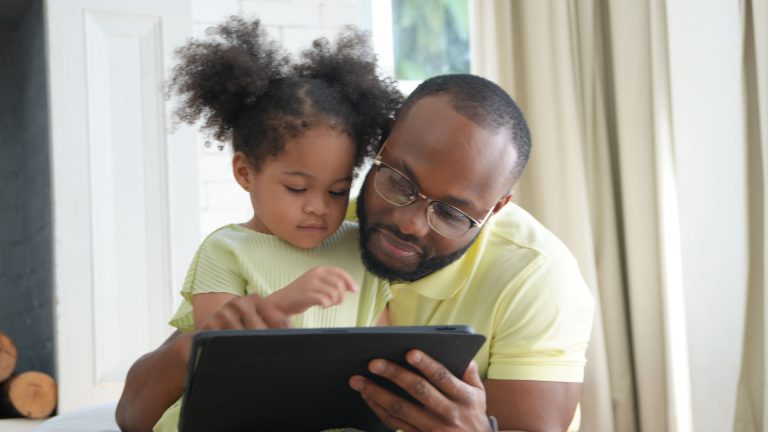 Father and child cuddle together looking at a tablet